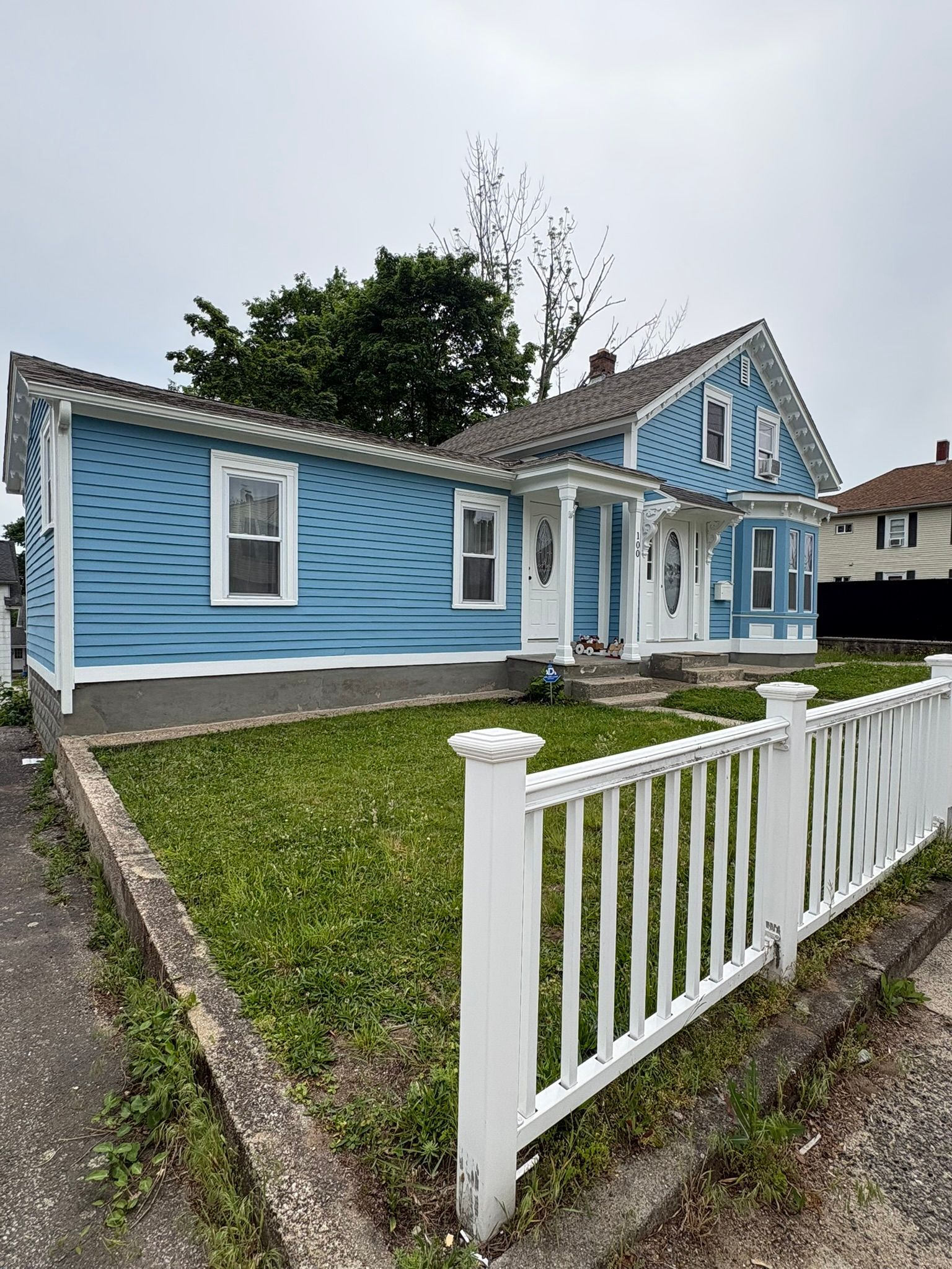 Blue house with white trim and a white fence along a grassy front yard