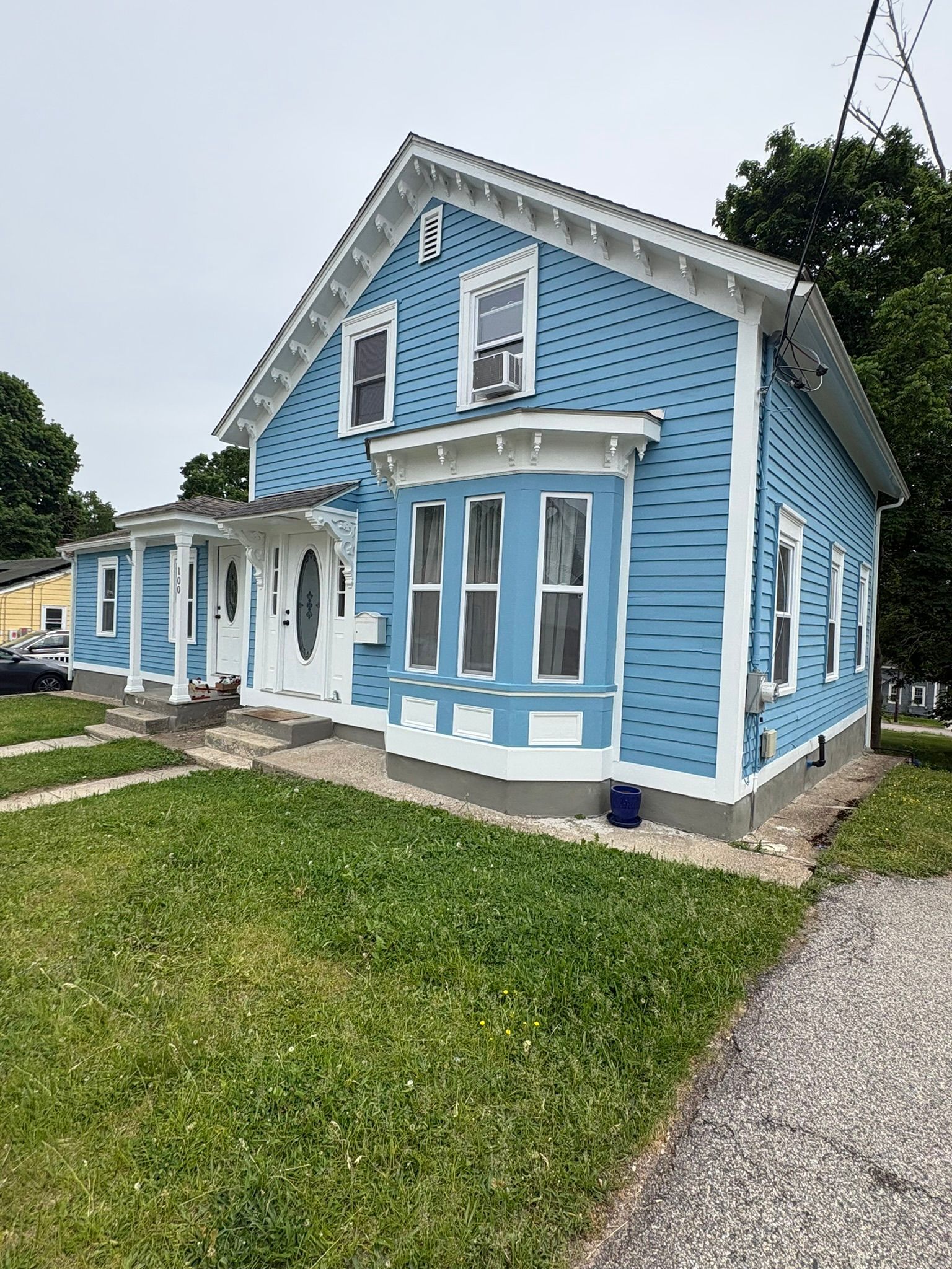 Blue Victorian-style house with white trim, bay windows, and a green lawn beside a gravel driveway
