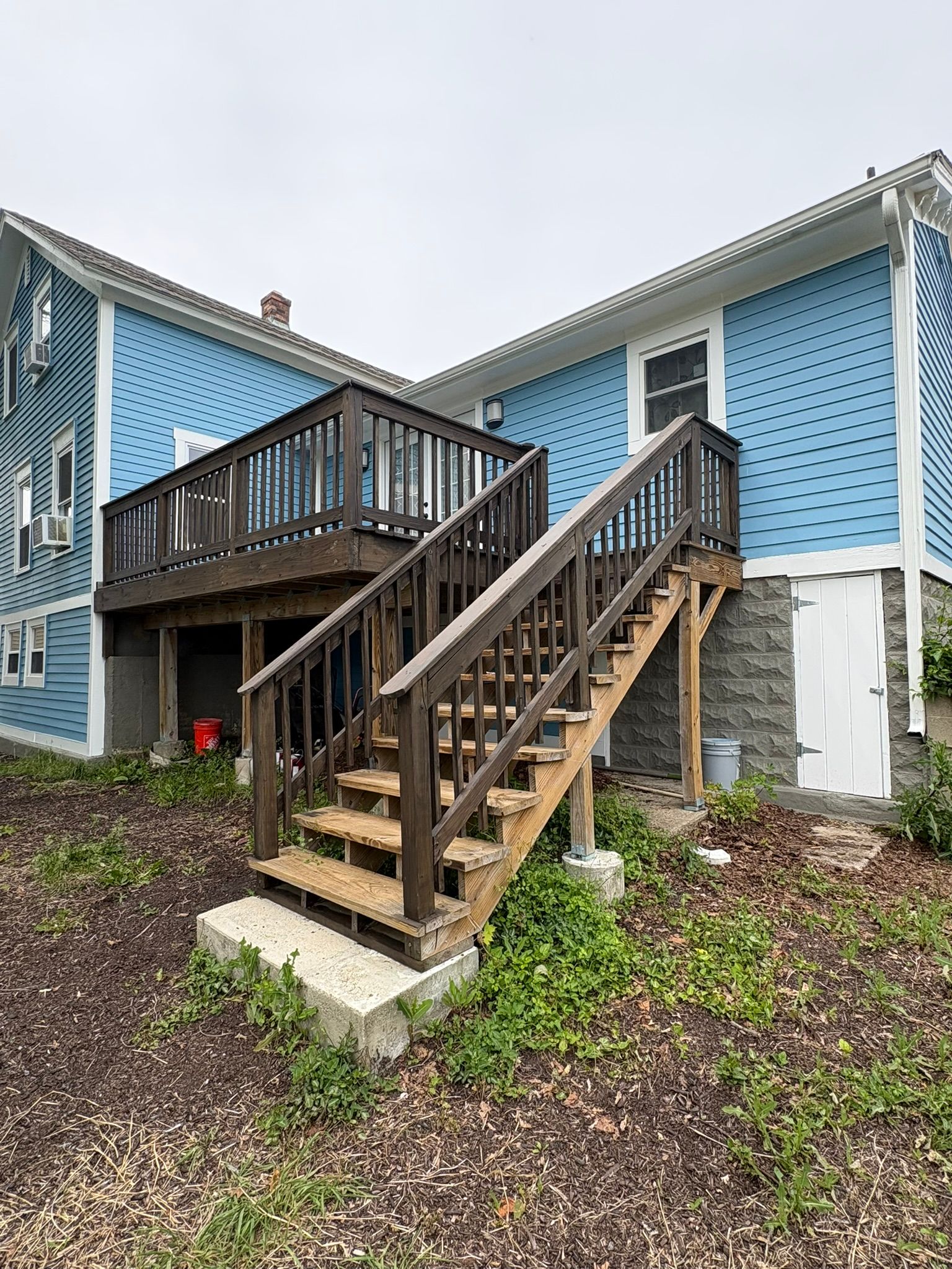 Blue house exterior with wooden stairs and deck leading to a side entrance