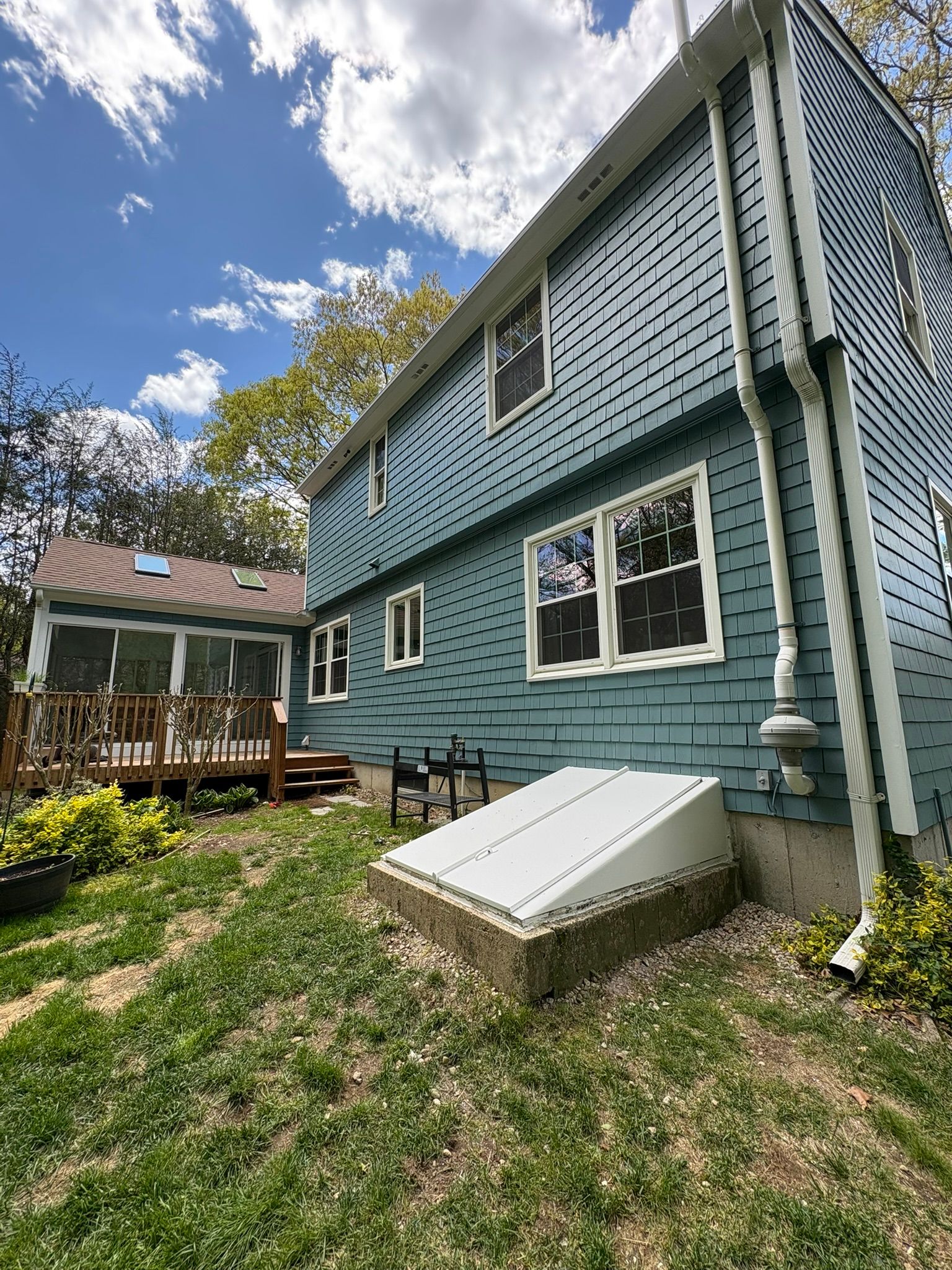 Blue house exterior with white-trim windows, sloped basement window, and a small porch under a partly cloudy sky