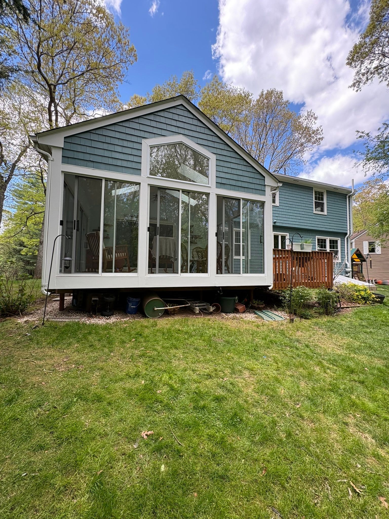Blue house with large screened porch, white trim, and green lawn under a partly cloudy sky