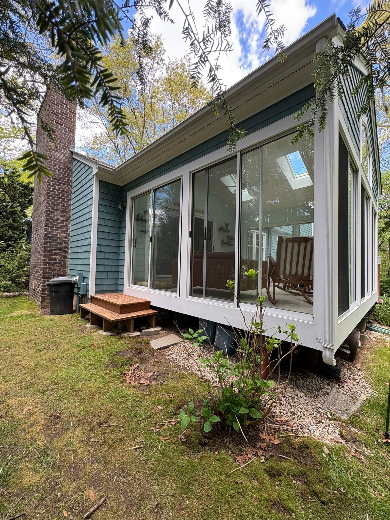 Small glass sunroom addition on a house, with white framing, brick chimney, and a grassy yard.