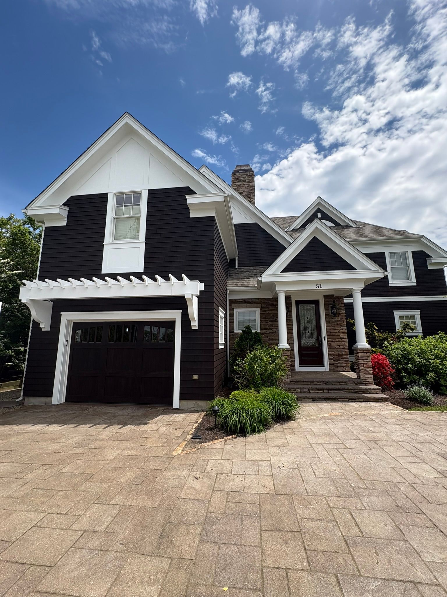 Suburban house with dark siding, white trim, garage, and a stone driveway under a blue sky