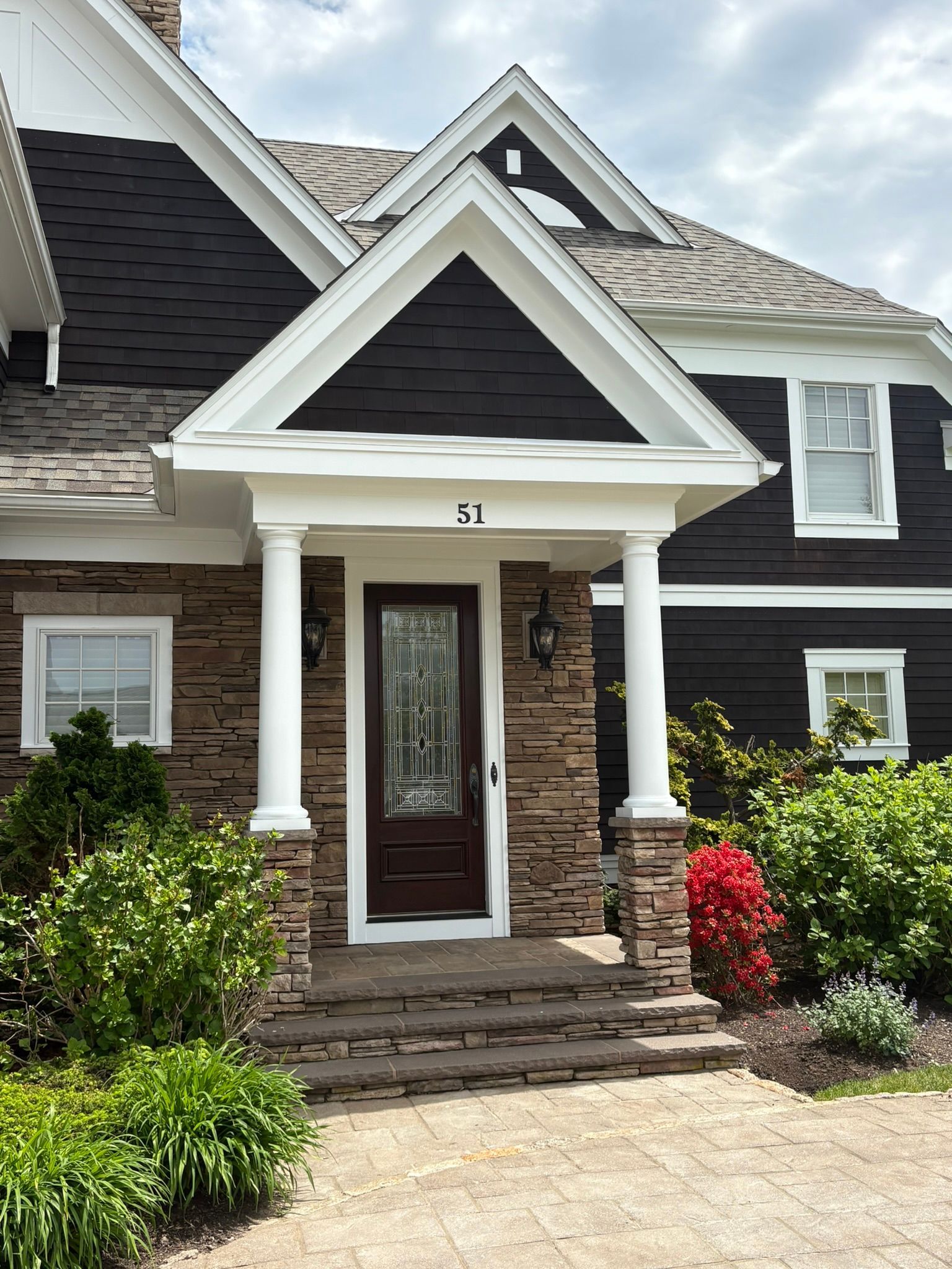 Front entrance of a dark gray house with white trim, stone steps, and landscaped shrubs