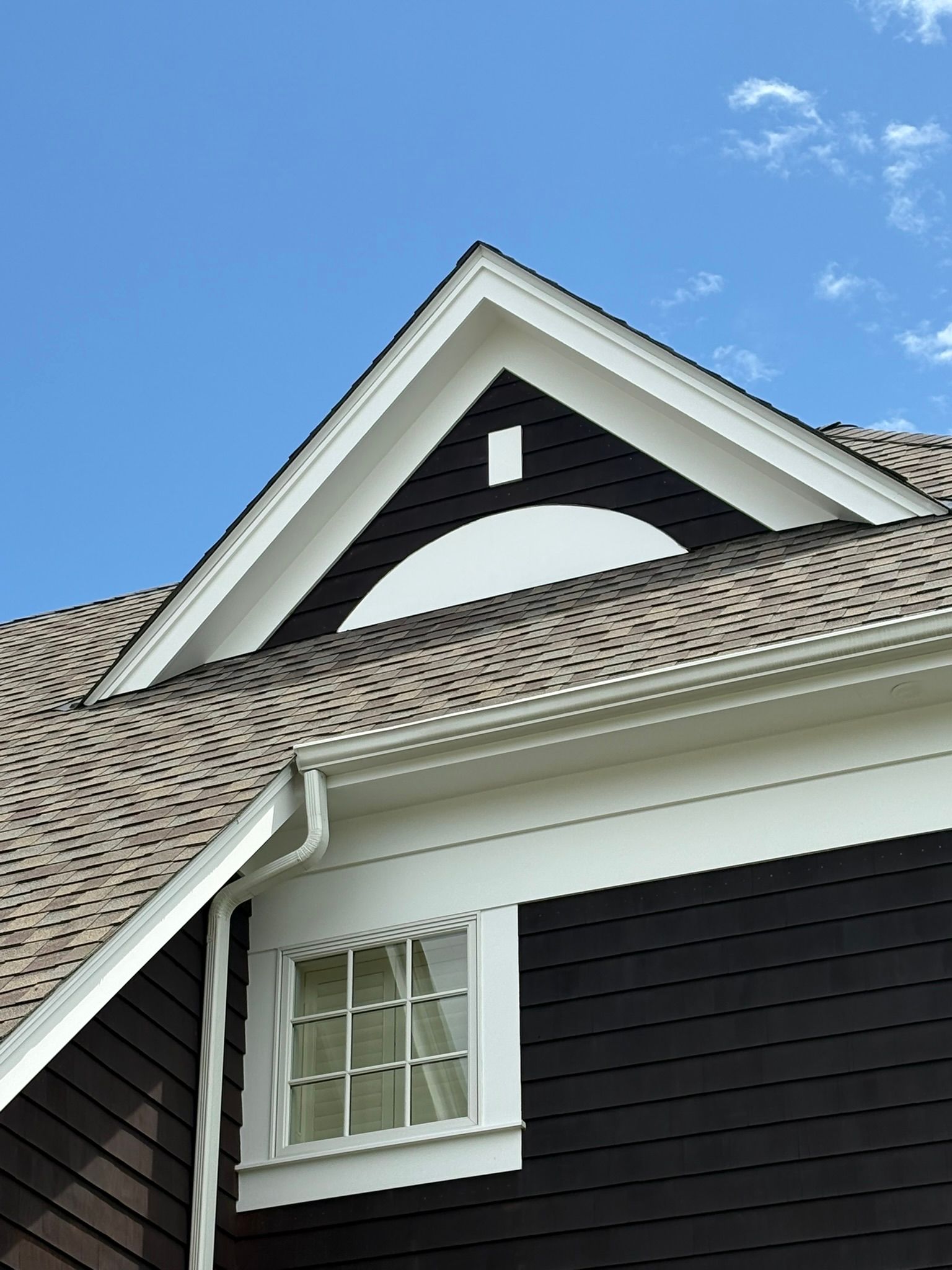 Exterior of a house roof with white trim, dark siding, and a dormer against a blue sky