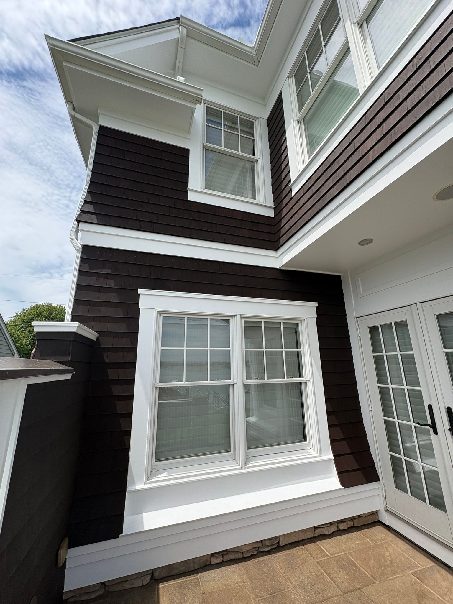Exterior of a dark shingle house with white trim, windows, and a glass door under a sloped roof