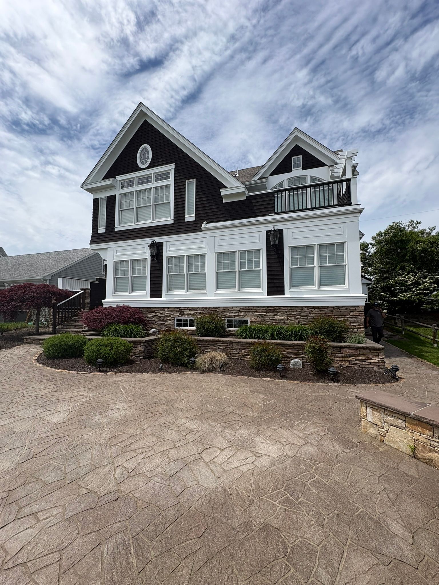 White two-story house with dark roof and large windows, fronted by gravel driveway and landscaped garden under cloudy sky