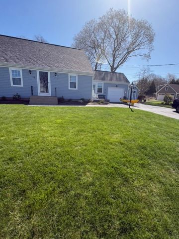 Suburban house with green lawn, leafless tree, and driveway under a bright blue sky