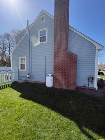 Blue house exterior with red brick chimney, white fence, and grass yard in sunlight