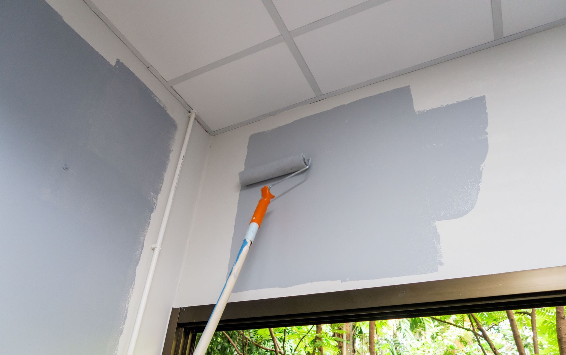 A person paints a wall gray with a roller. White ceiling and trim.