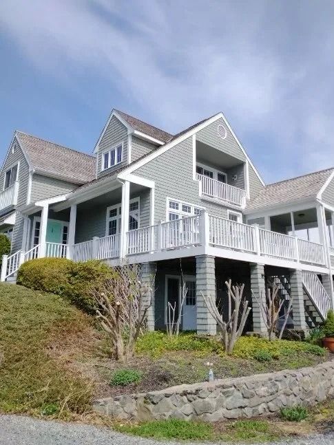 Grey house with white balconies, set on a hillside, against a blue sky.