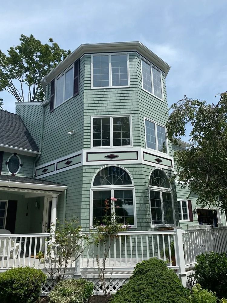 Green house with tower of windows, white trim and deck, against a cloudy sky.