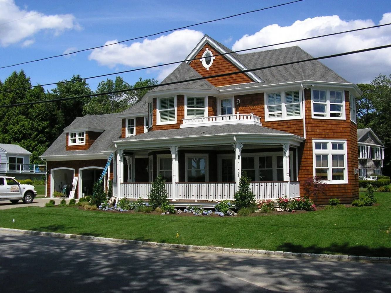 Two-story house with cedar shingles, white trim, porch, and attached garage on a grassy lot.