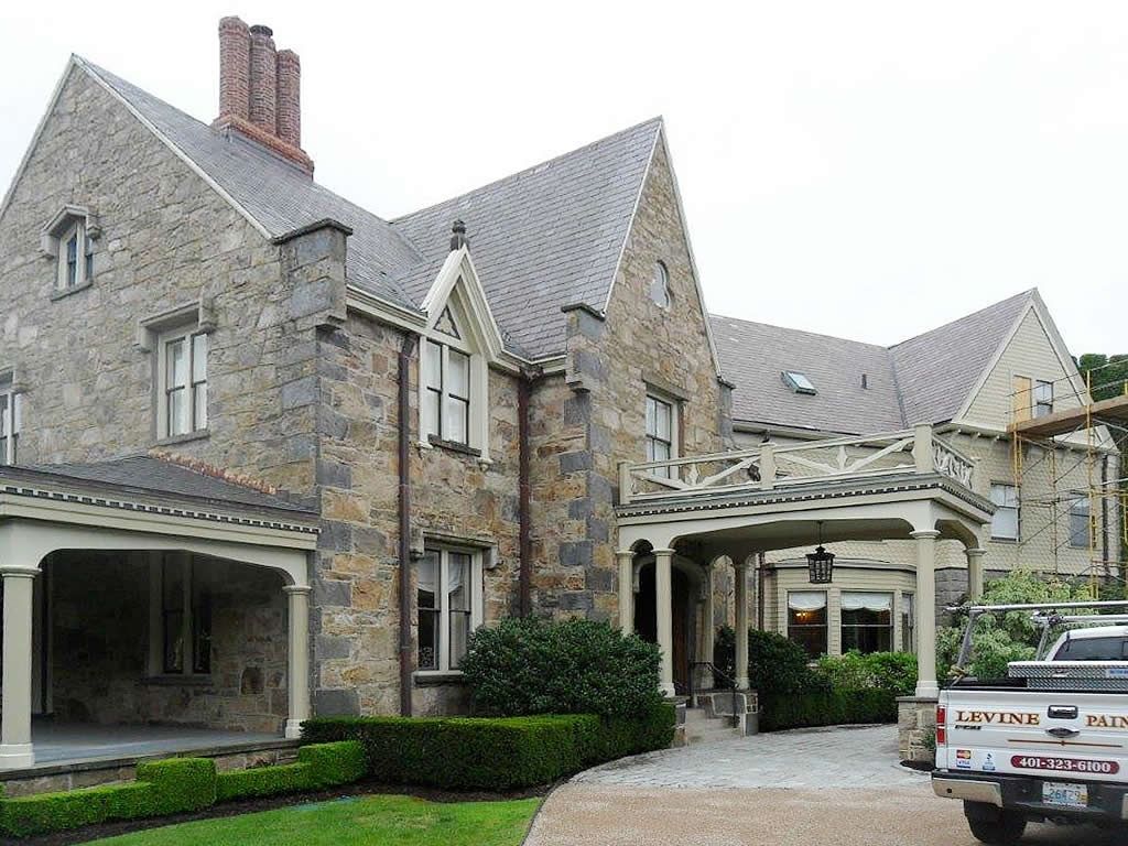 Stone mansion with slate roof, arched entry, and pergola-covered entrance. A truck is parked to the right.