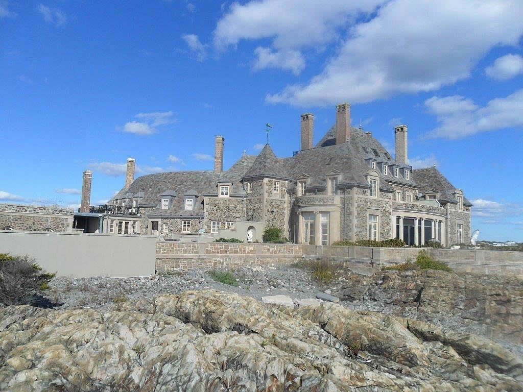 Stone mansion on a rocky coast with a blue sky and scattered clouds.