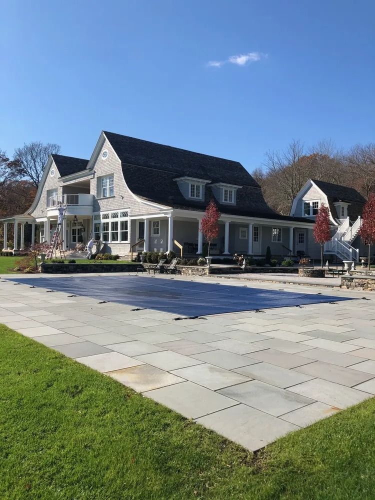 Large gray house with a curved roof, white trim, and a covered pool on a sunny day.