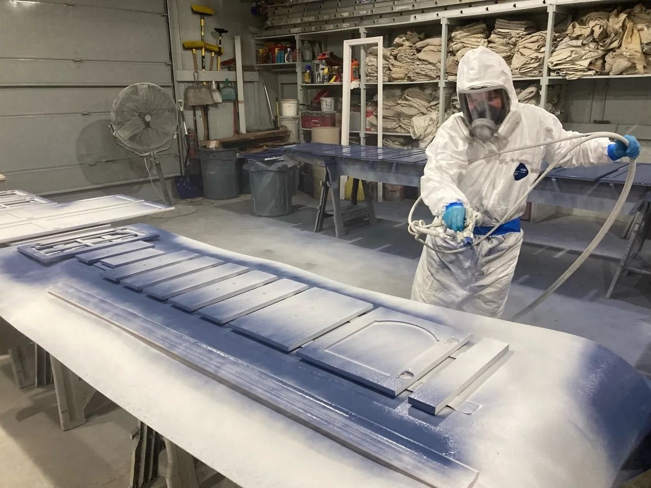 Person in protective suit spraying paint on furniture in a workshop.