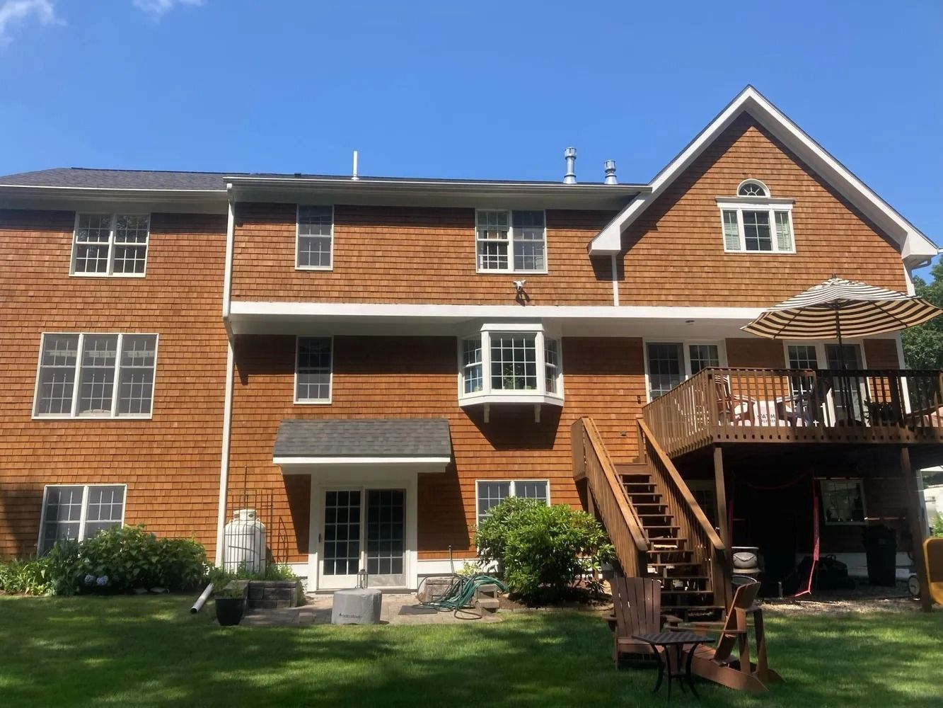 Brown house exterior with windows, deck, and green lawn under a blue sky.