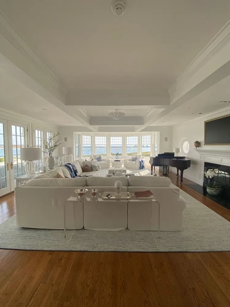 Spacious white living room with ocean view, sectional sofa, piano, fireplace, and hardwood floors.