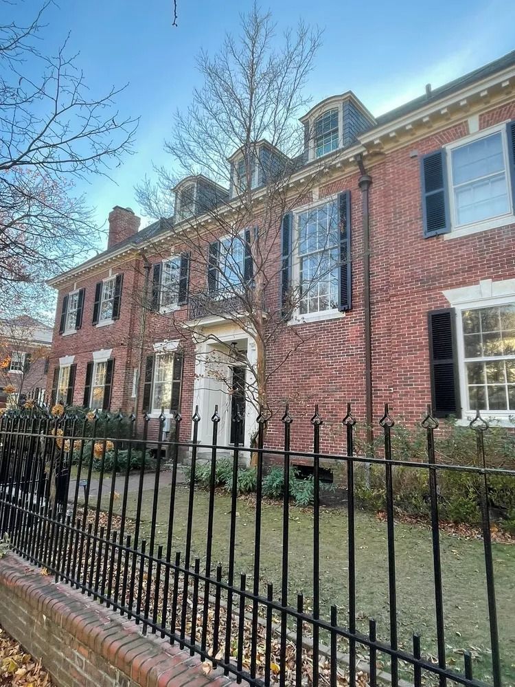 Red brick building with black shutters, a white doorway, and black wrought-iron fence.