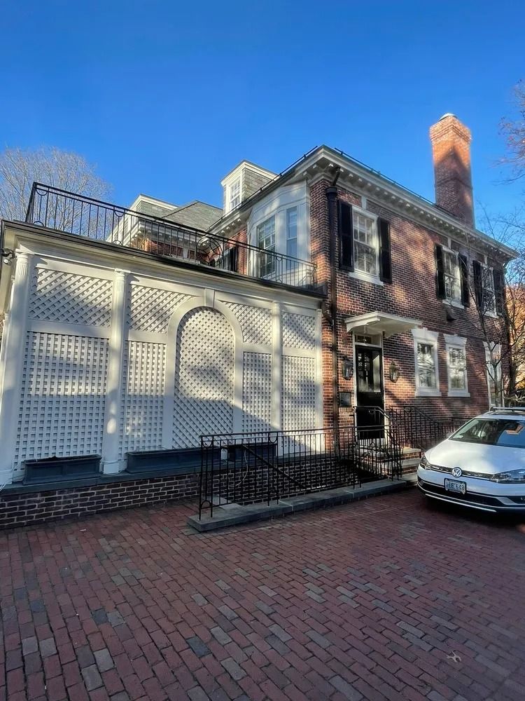 Red brick house with black shutters, white lattice wall, and a brick driveway on a sunny day.