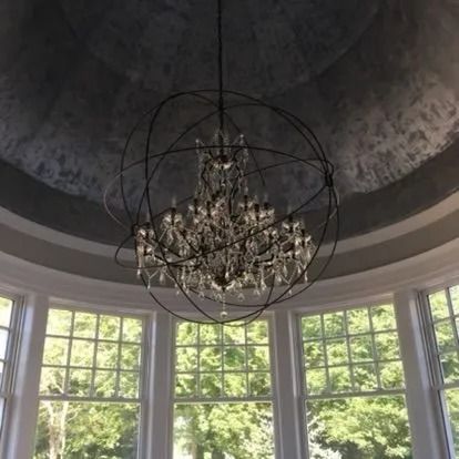 Chandelier in a circular, window-filled room with a textured gray ceiling.