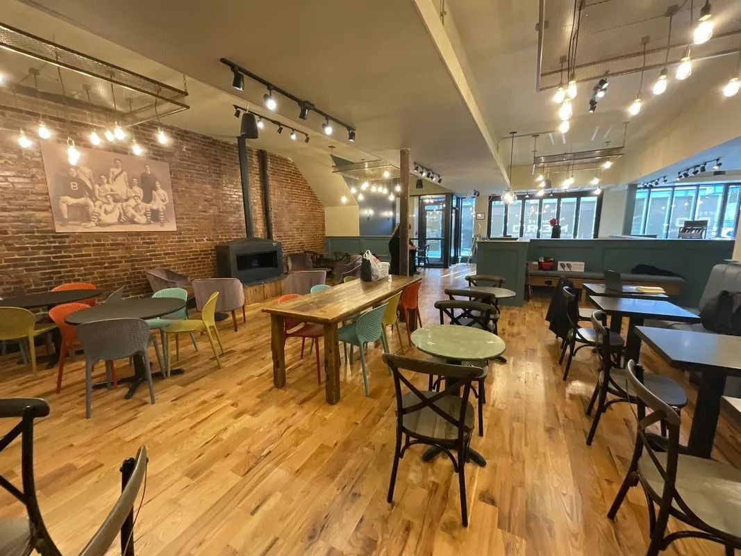 Interior of a cafe with wooden floors, brick walls, tables, chairs, and string lights.