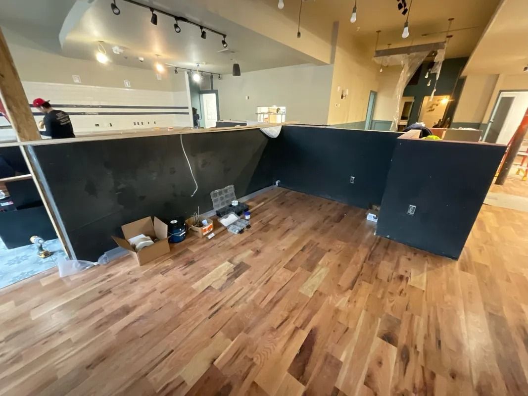 Interior with unfinished wood floors, dark counter, boxes, and tools; appears to be a renovation in progress.