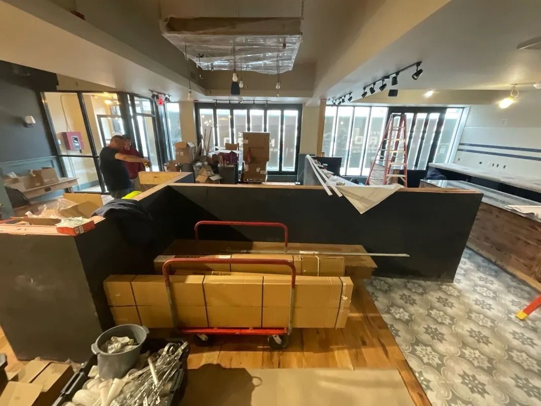 Interior of a business under construction with workers, materials, and exposed brick.