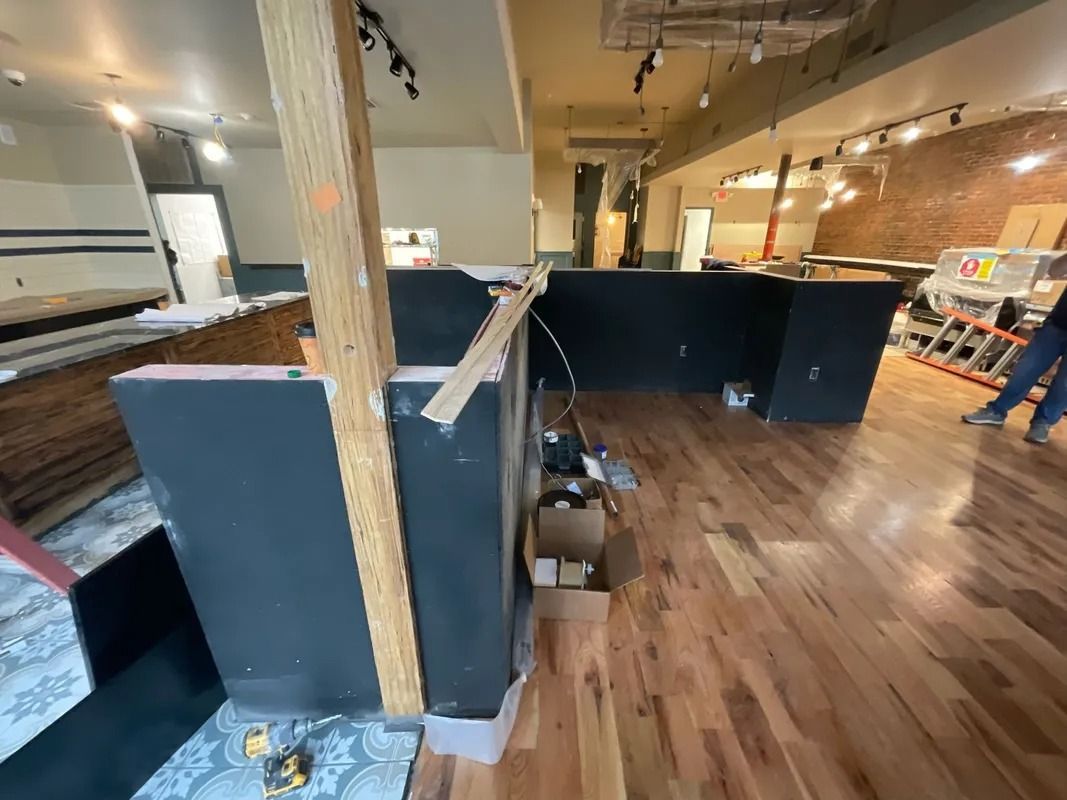 Interior construction: wooden beams, black counters, hardwood floor, exposed brick wall, and tools.