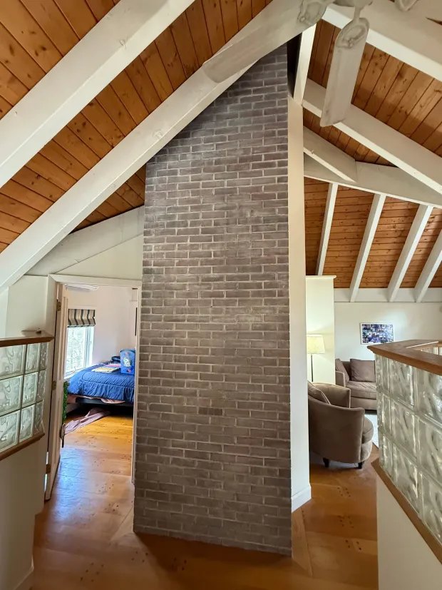 Brick chimney bisecting hallway with wood ceiling and floors. Glass block railings.