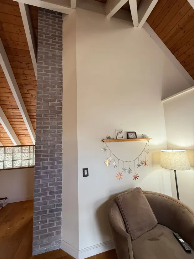 Interior with brick column, white walls, wood ceiling, and a sitting area with a lamp.