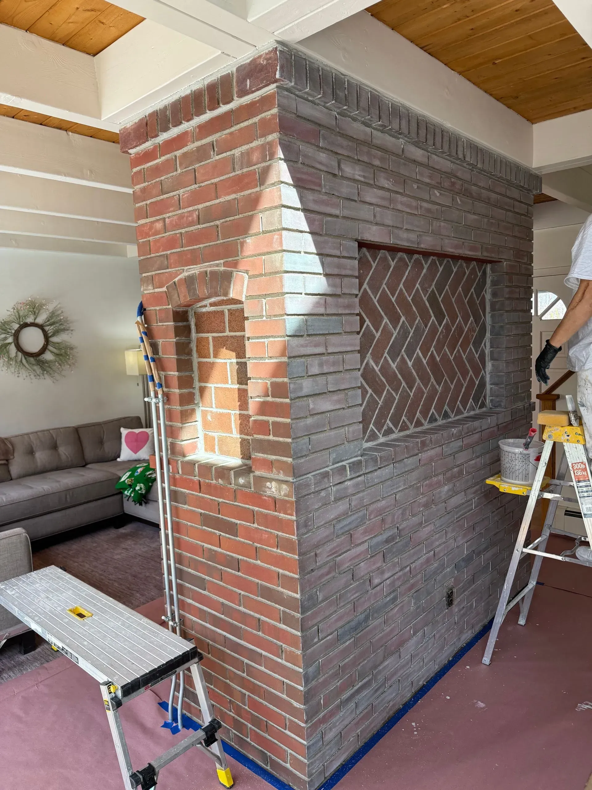 Brick wall being painted grey by a person on a ladder; living room setting.
