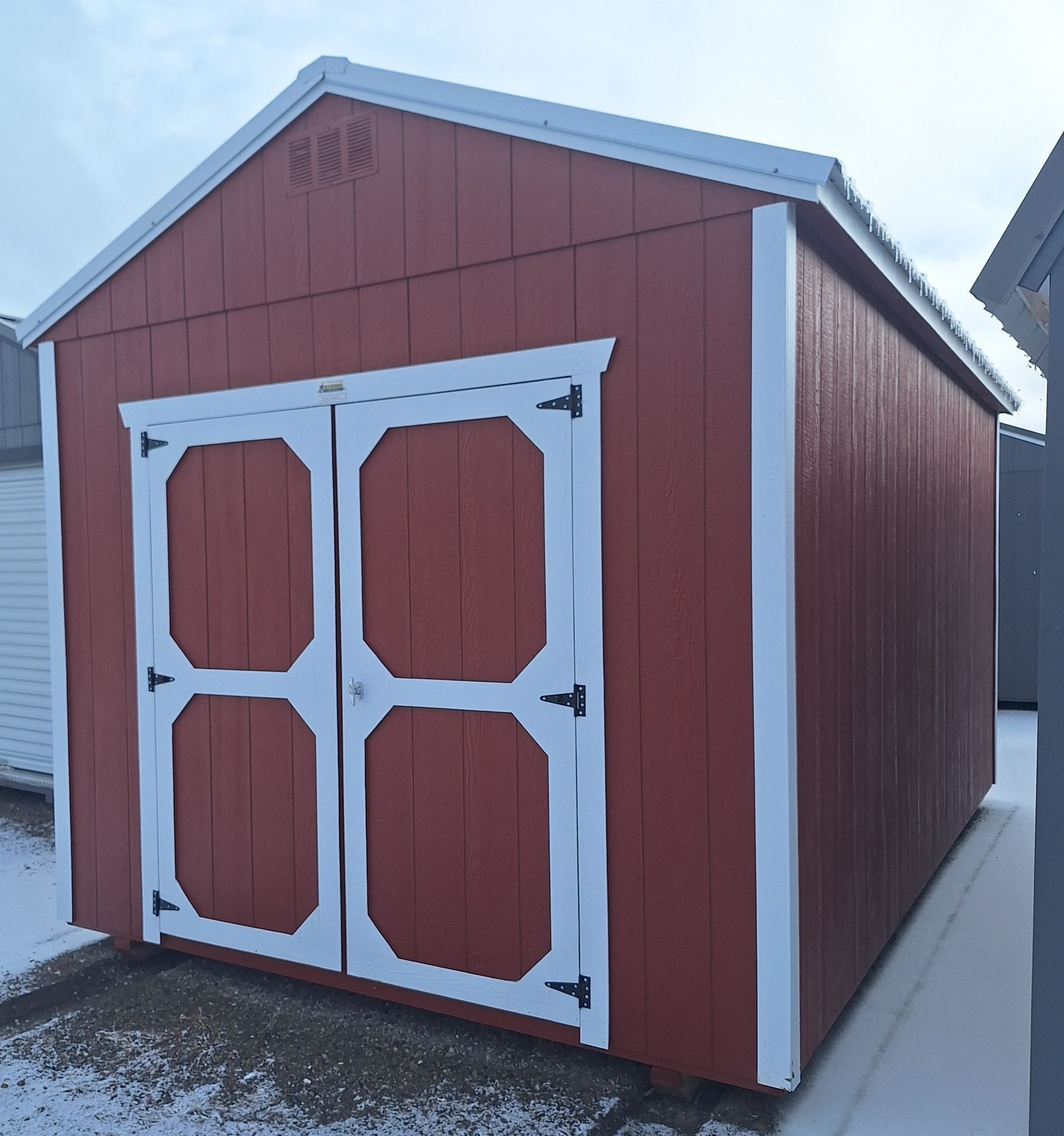 A light blue, wooden storage shed with a single door, a gable roof, and a vent, sitting on a gravel lot.