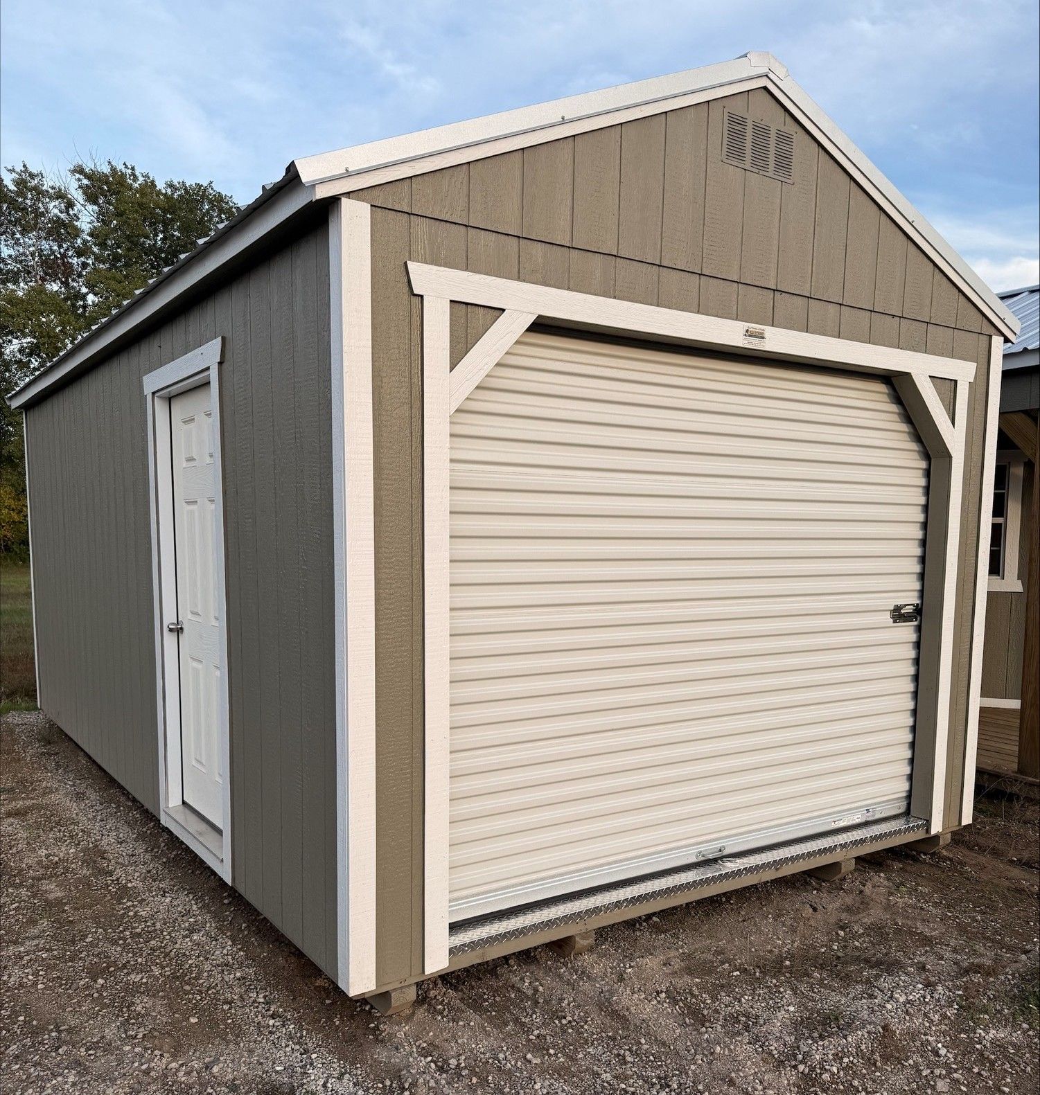 A gray, rectangular storage shed with a white trim, a roll-up garage door, and a side access door, set on a snowy surface.