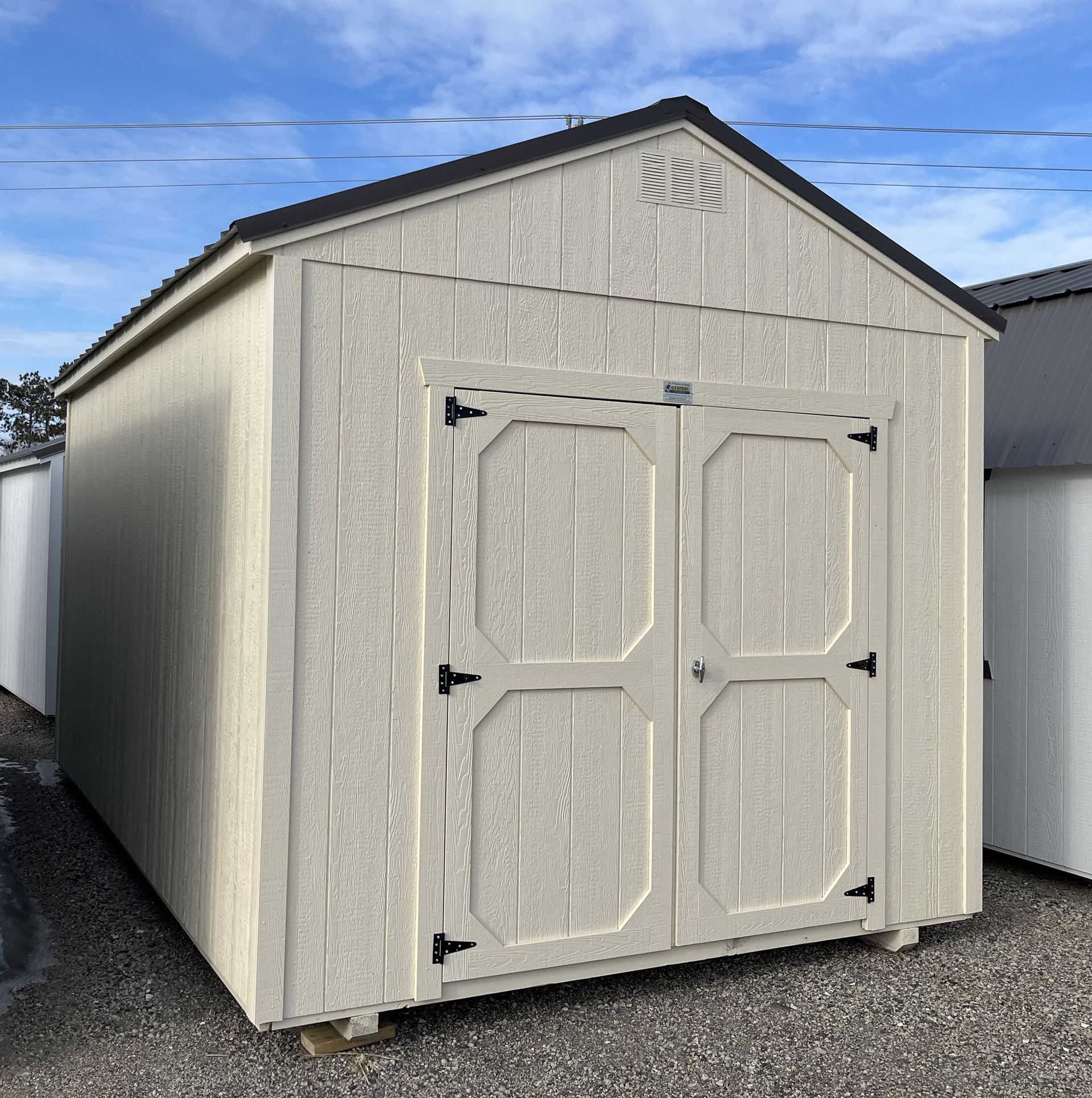 Tan shed with a black roof and double doors against a blue sky.