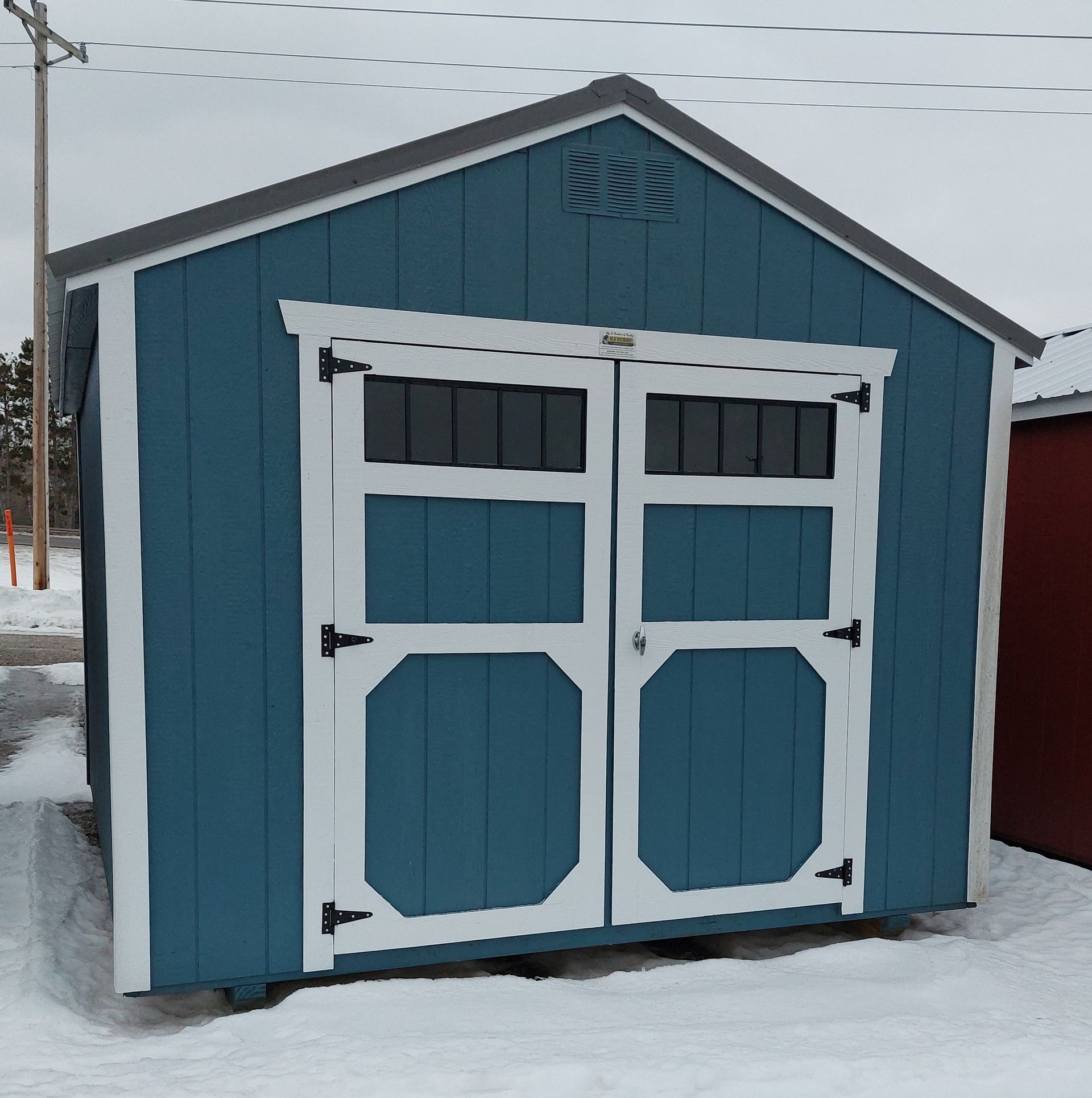 A blue wooden shed with white trim and double doors, sitting outside in a snow-covered area.