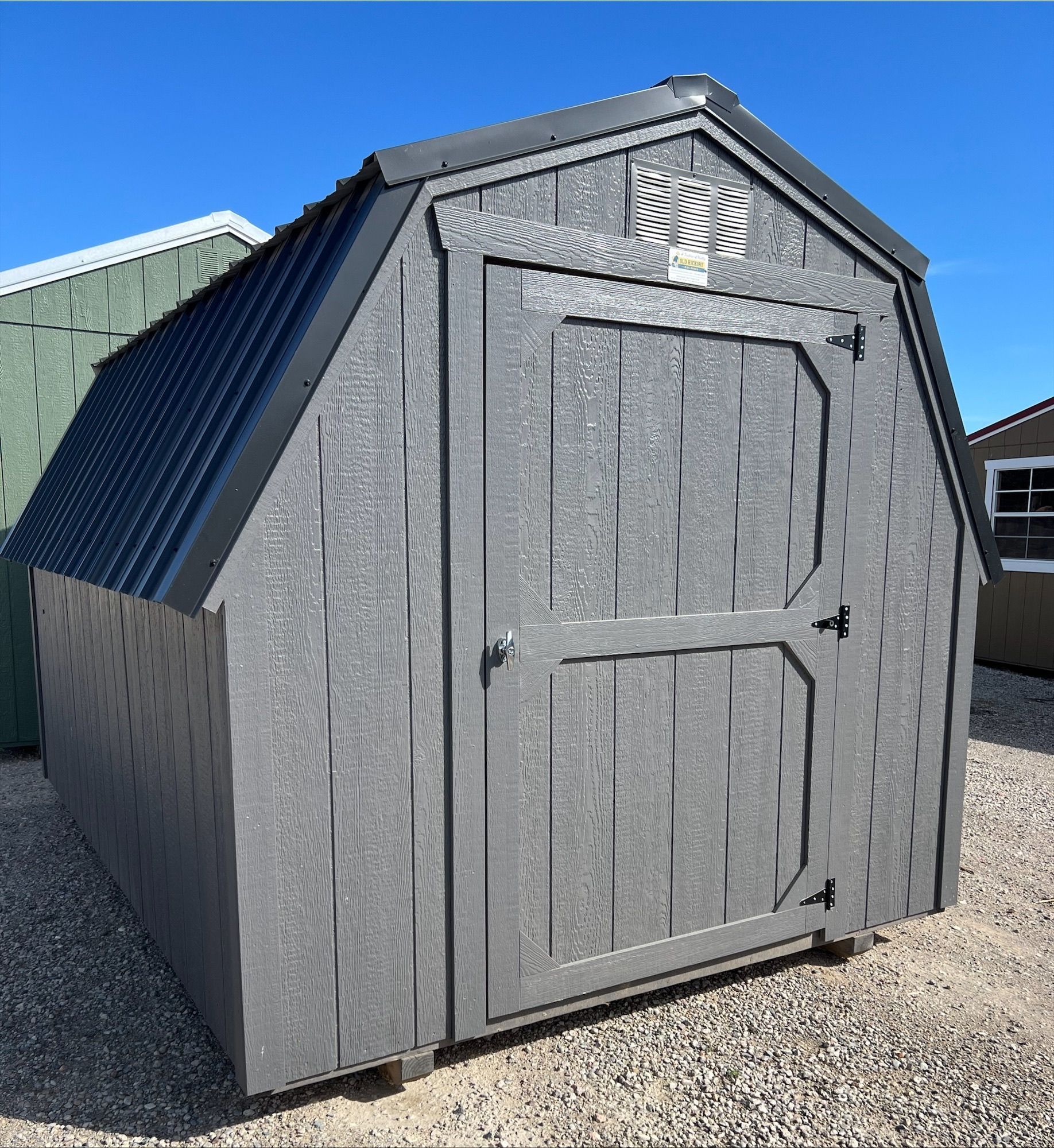 A red wooden storage shed with cream trim, a single window, and double doors, standing on a grassy outdoor lot.