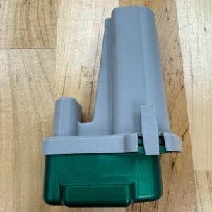 A two-tone object, green base with a gray top, sits on a wooden surface.