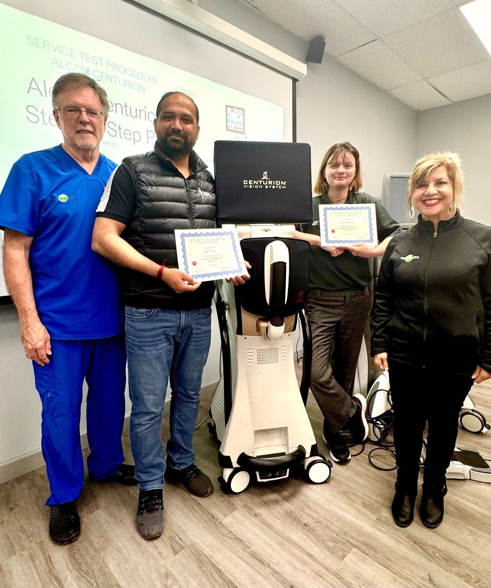 Four people pose with certificates next to a medical device in a room.