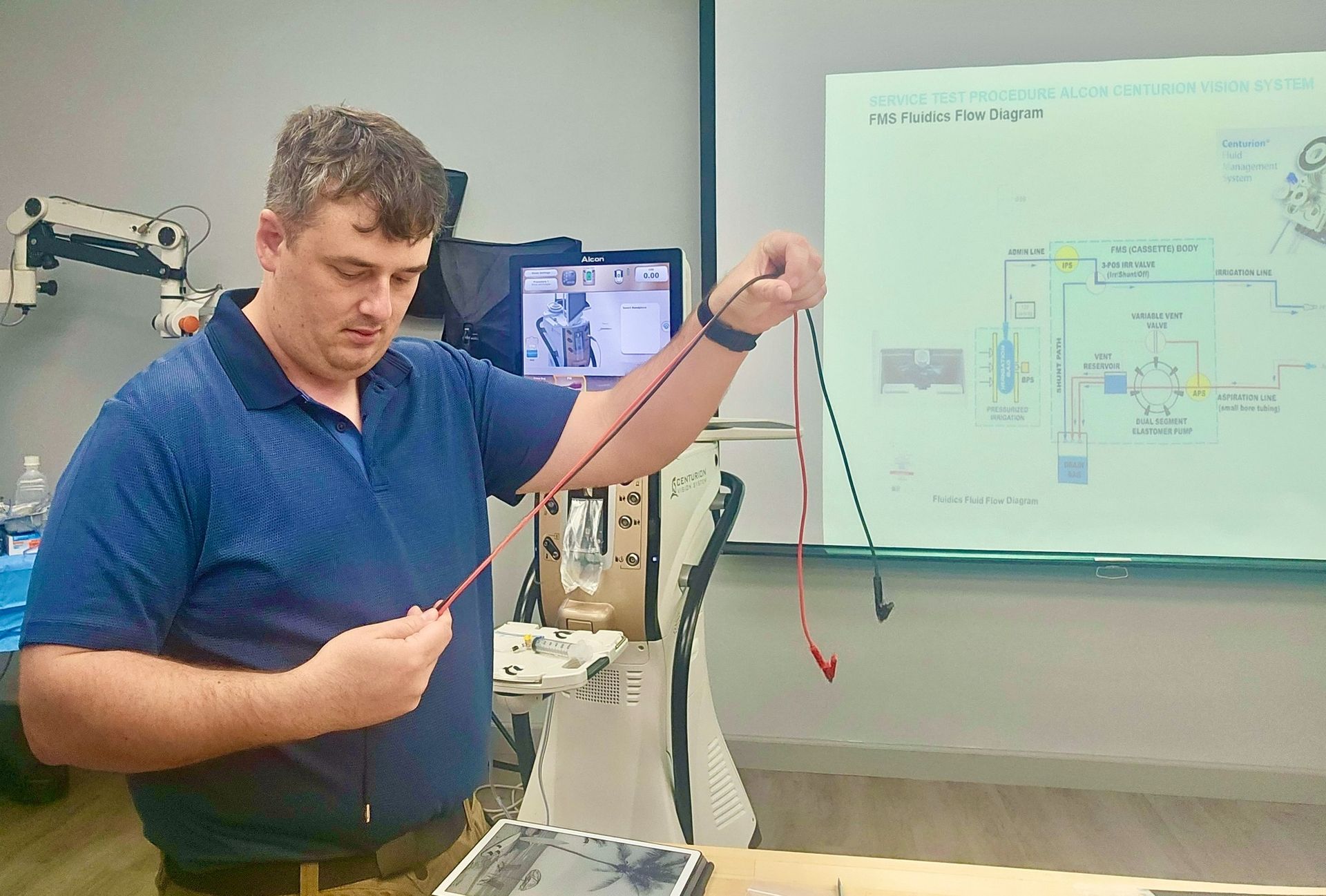Man demonstrating wires in a medical training room, holding red and black cords.