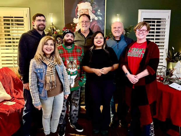 Group of people smiling at a Christmas gathering with a Santa painting in the background.