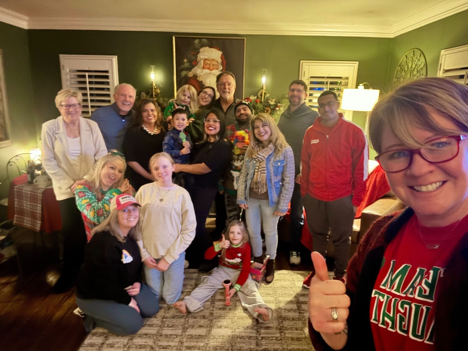 Group of people smiling, posing for a photo. Christmas decorations in the background, including a Santa painting.