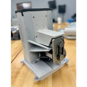 Silver industrial machine with a rectangular base and a box-like top section, set on a wooden surface.