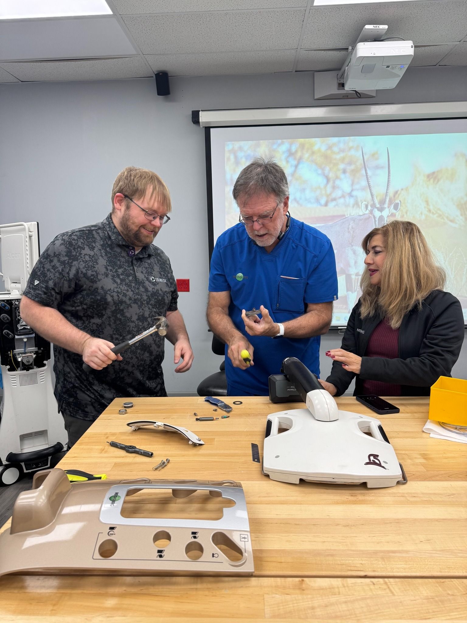 Three people assembling a device at a workshop table.