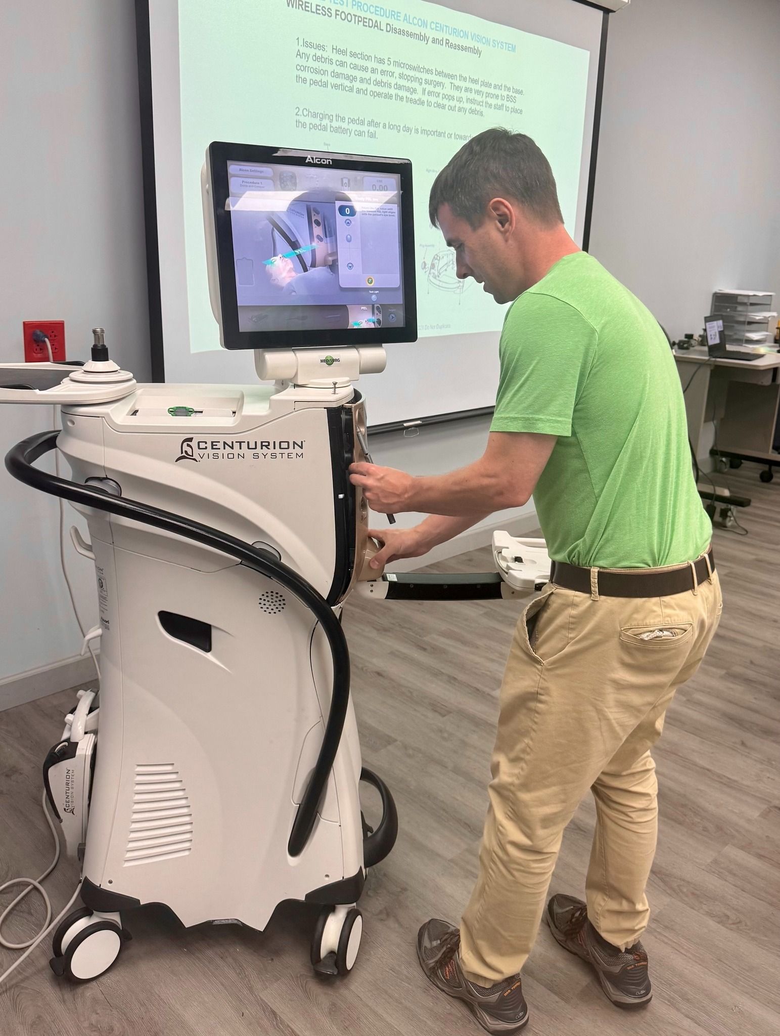 Man operating medical device with screen in a room, a presentation in the background.