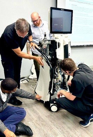 Three people kneel around a robot in a lab, adjusting its wiring near a monitor.