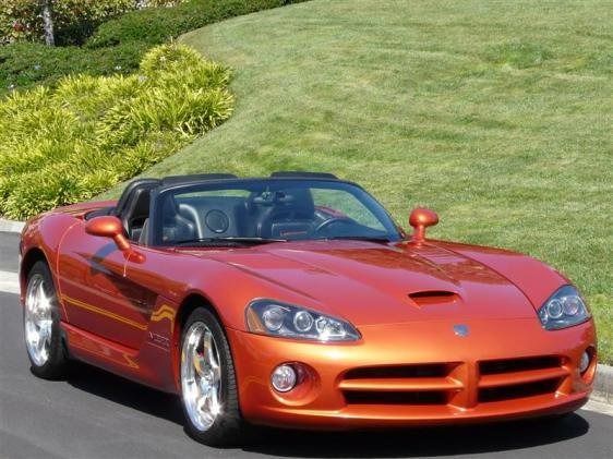 Orange Dodge Viper convertible on a road, with green grass and bushes in the background.