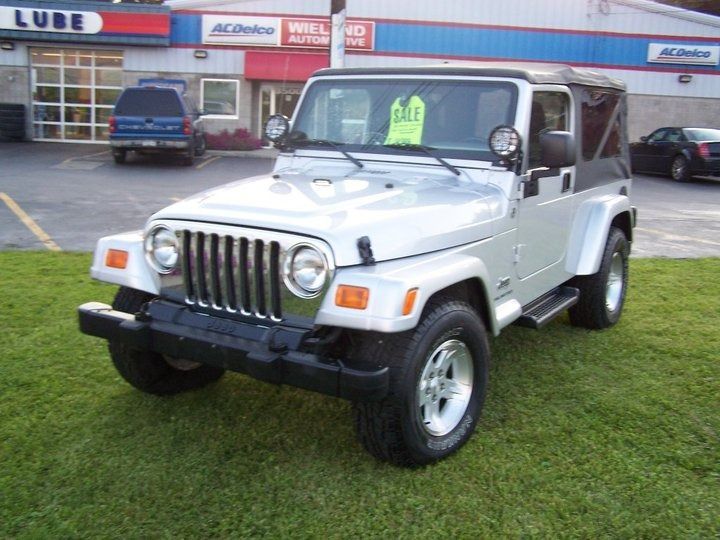 Silver Jeep Wrangler parked on grass in front of an auto shop.