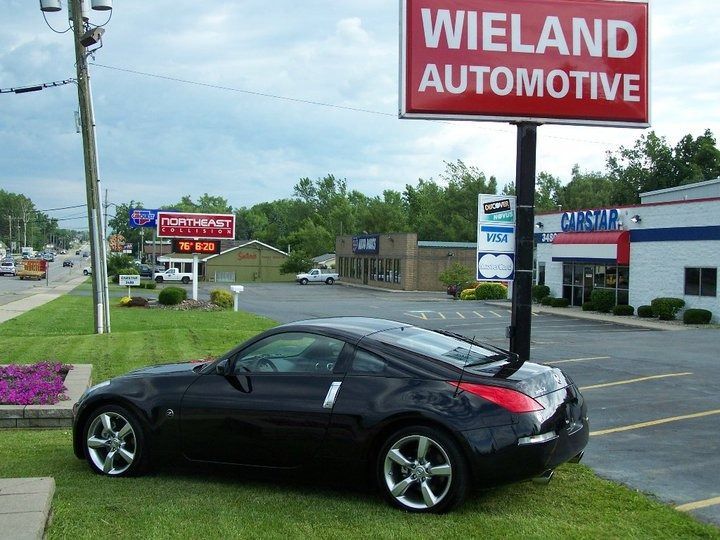 Black sports car parked on grass in front of Wieland Automotive sign.